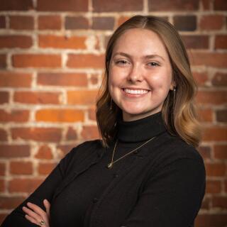 Picture of a woman in a black shirt leaning against a brick wall.