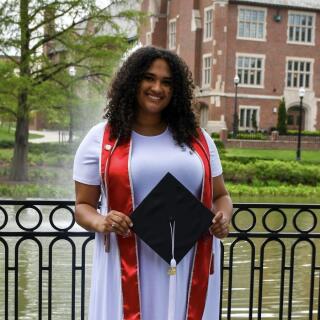 Woman in a white dress holding a graduation cap outside.