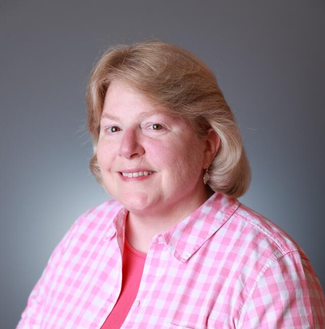 Picture of a woman in a pink collared shirt with a blue background.