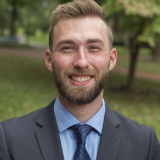 Headshot of a man in a suit with a blue shirt and tie.