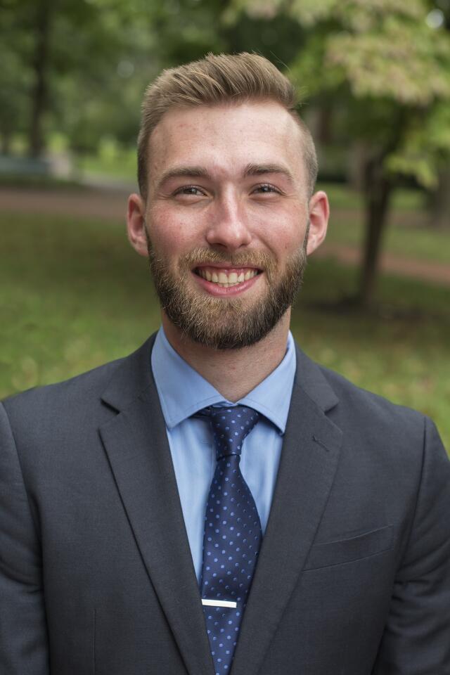 Headshot of a man in a suit with a blue shirt and tie.