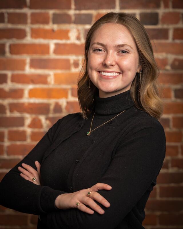 Picture of a woman in a black shirt leaning against a brick wall.