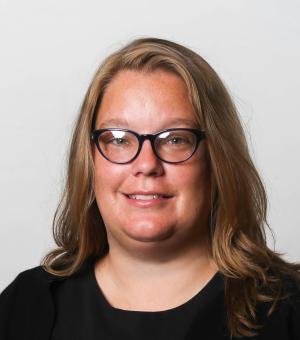 Headshot of a blonde woman with glasses dressed in black.
